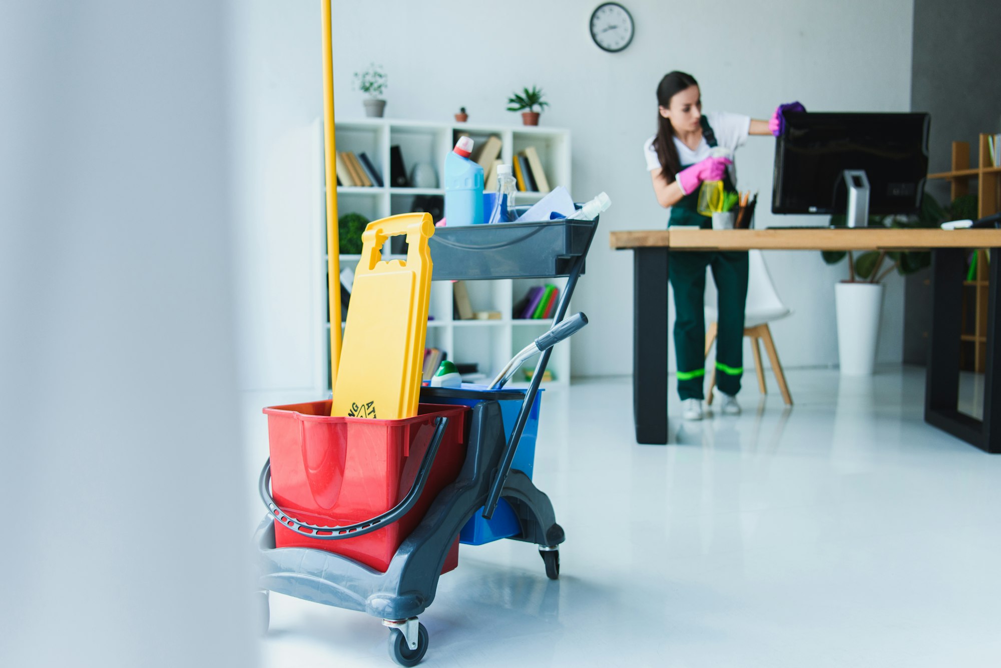 young female janitor cleaning office with various cleaning equipment